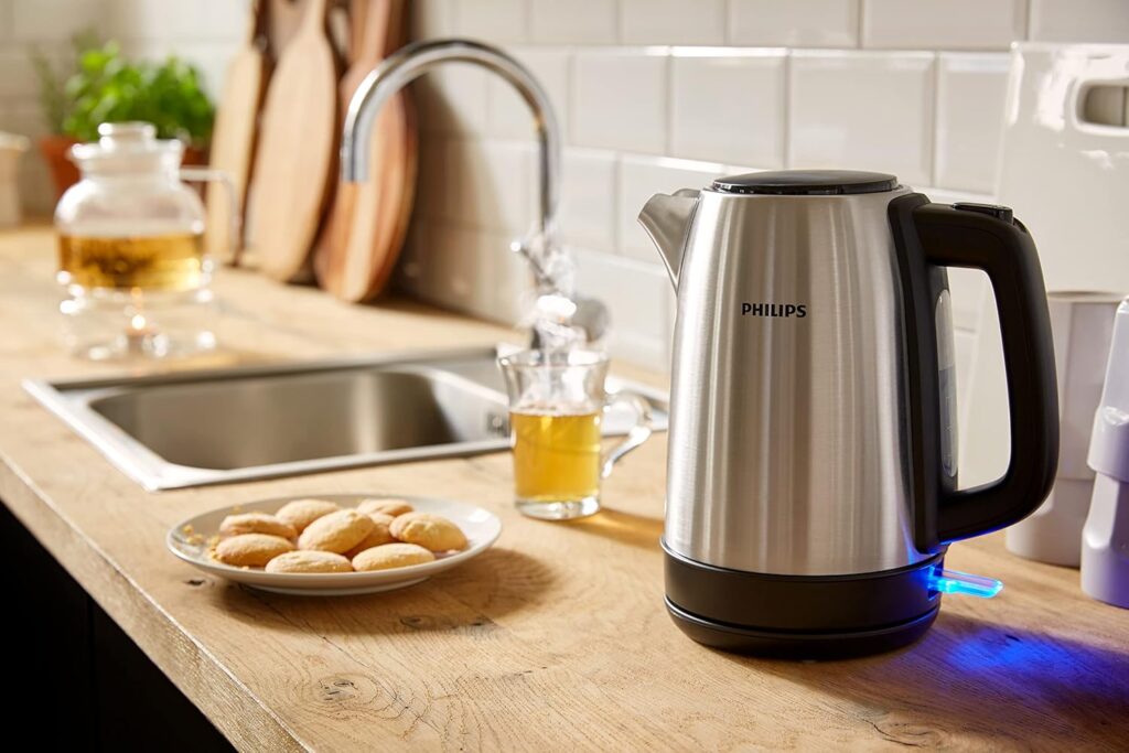 Philips stainless steel electric kettle HD9350 with illuminated blue power indicator on a wooden kitchen counter next to tea and cookies
