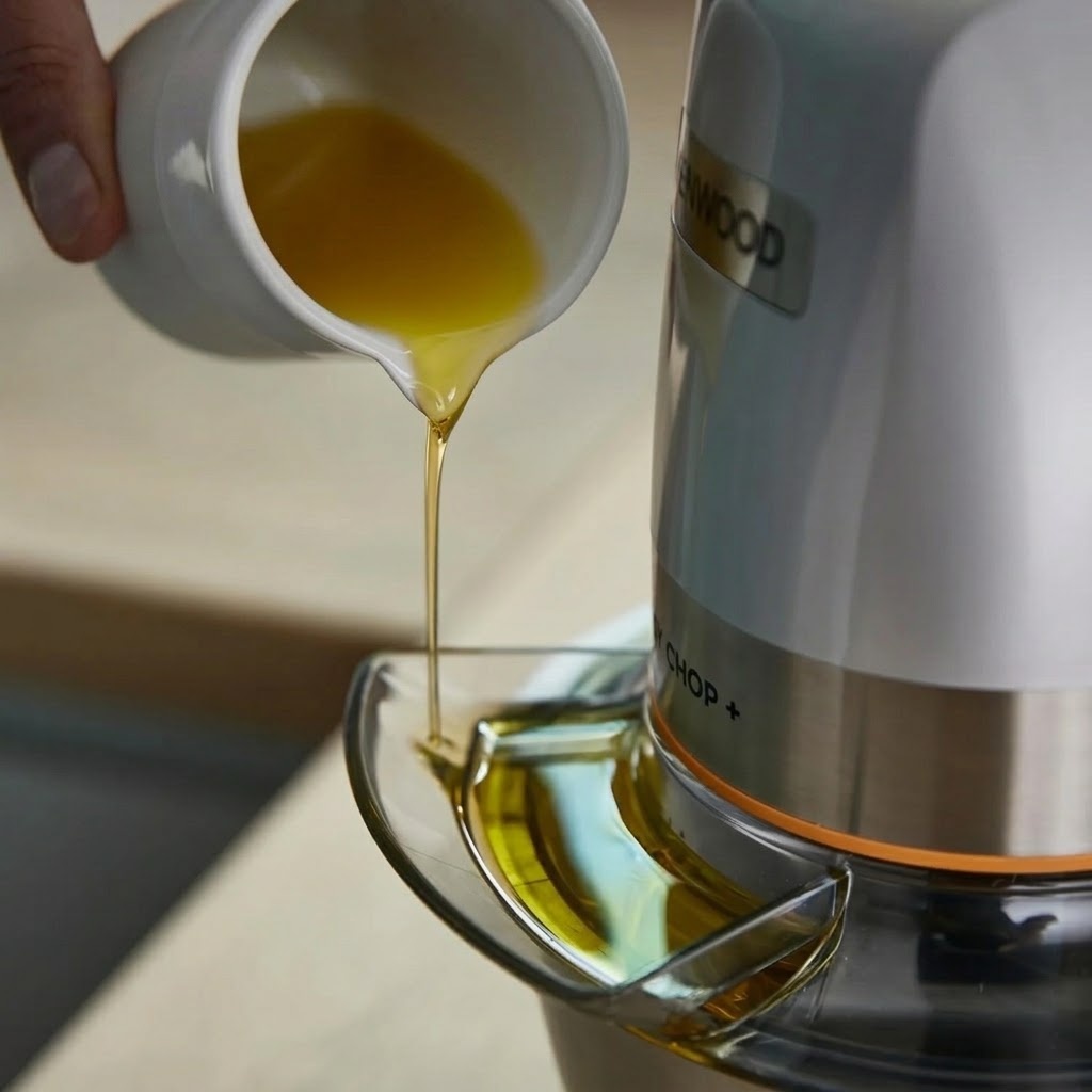 Close-up of olive oil being poured into the Dripper Pro lid attachment of a Kenwood Easy Chop+ CHP62.400 mini food chopper to make dressings and sauces.