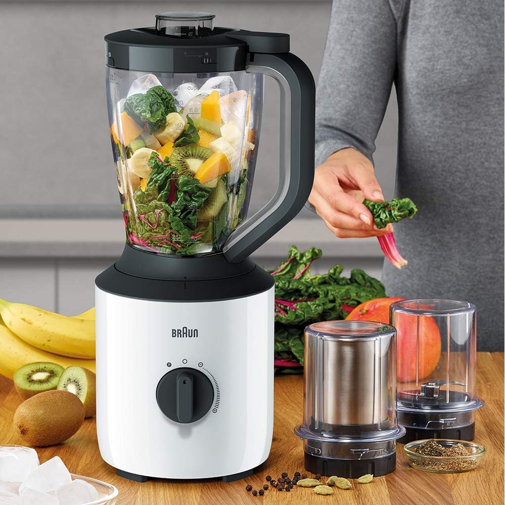 Braun PowerBlend 3 JB3123 white blender on a kitchen counter next to chopper and grinder attachments, surrounded by fresh fruits, leafy greens, and spices.