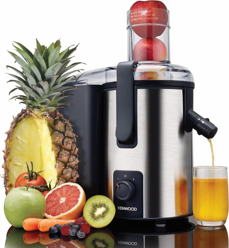 Kenwood JEM50 700W stainless steel centrifugal juicer extracting fresh juice into a glass alongside mixed fruits including pineapple, apples, grapefruit, kiwi, and berries.