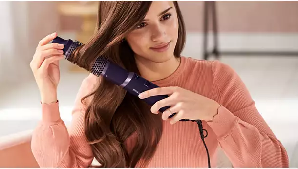 امرأة مبتسمة تحمل مصفف الشعر Philips 3000 Series BHA305 بشكل أفقي لتشكيل تجعيدات ناعمة وكثيفة باستخدام الفرشاة الحرارية.