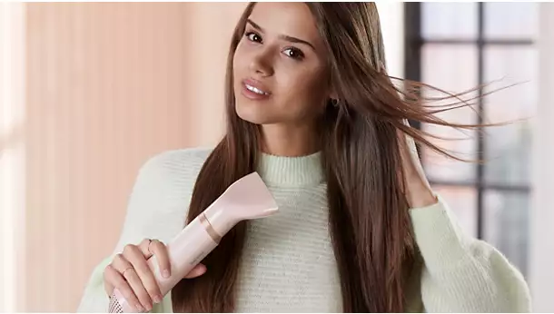 امرأة تجفف شعرها البني الطويل باستخدام مصفف الشعر Philips BHA310 بقوة 800 وات مع ملحق فوهة تركيز الهواء الضيقة.