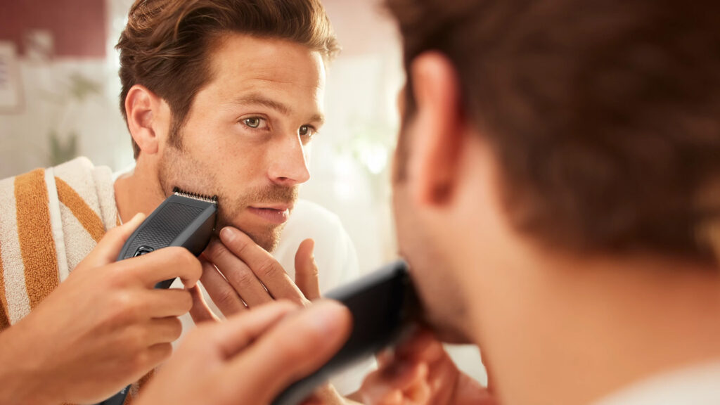Man looking into a mirror while trimming his beard using the Philips Hair Clipper Series 3000 HC3525 in a bathroom setting.