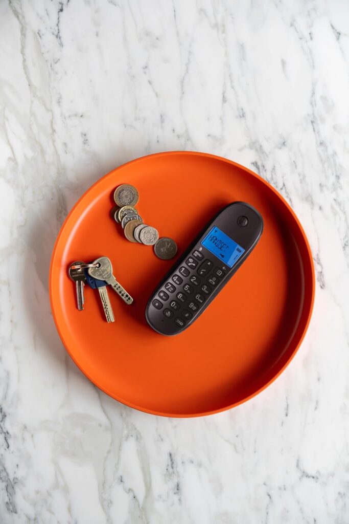 Motorola C1001CB+ cordless phone handset resting on an orange tray next to keys and coins